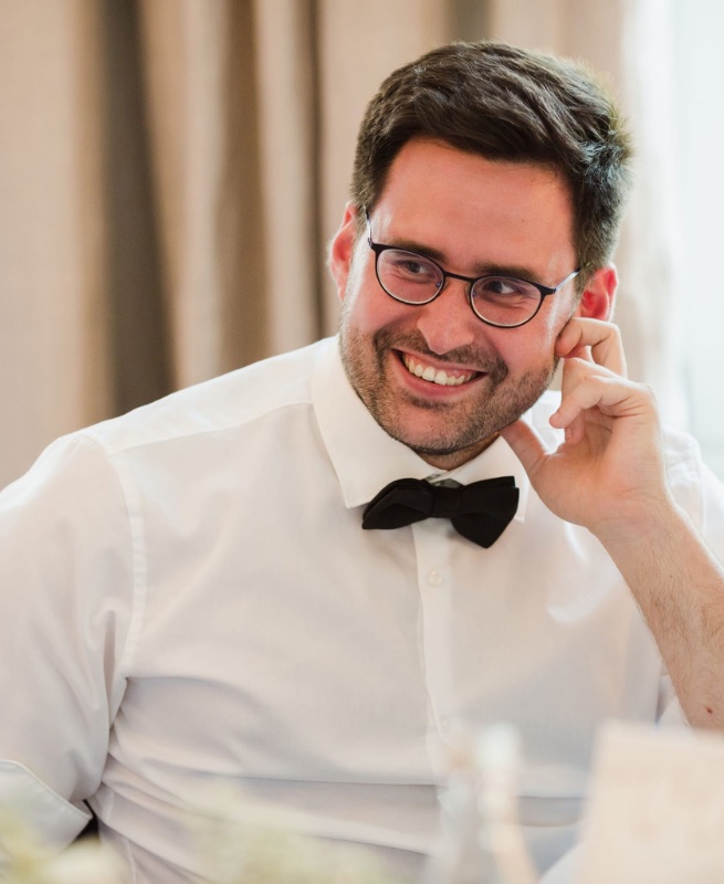 Sebastian Schmidt guckt lächelnd zur Seite. Er hat kurzes, dunkles Haar und trägt eine runde Brille. 